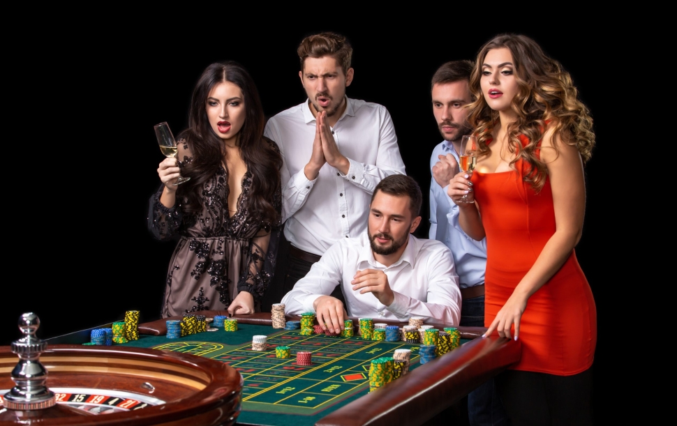 Group of young people looking excited at spinning roulette. Roulette table in a casino. Black background